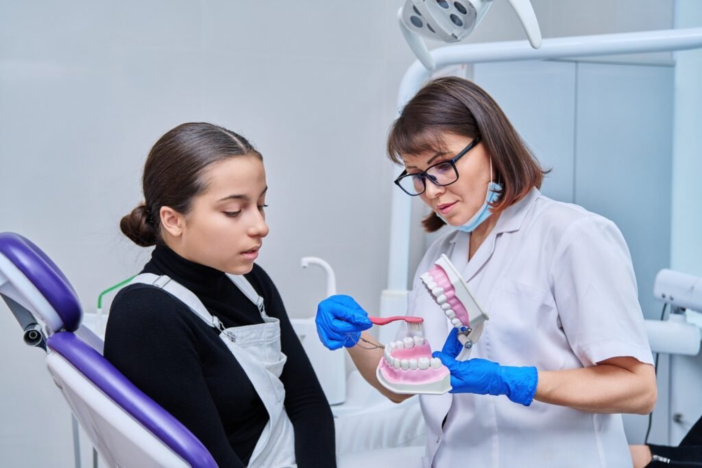 teenage female sitting in dental chair doctor with jaw model and toothbrush